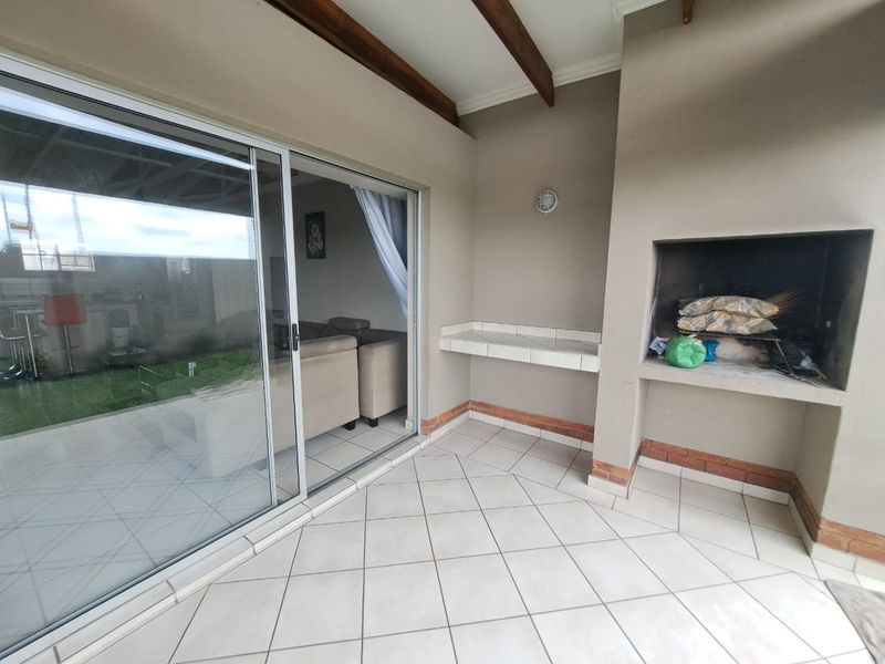 Covered patio area featuring a built-in braai, tiled flooring, and direct access to the living space through large sliding glass doors.
