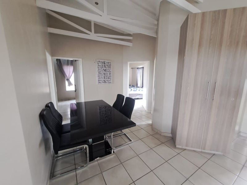 Open-plan living area featuring tiled flooring, exposed ceiling beams, and a built-in storage cupboard, providing access to adjacent rooms.