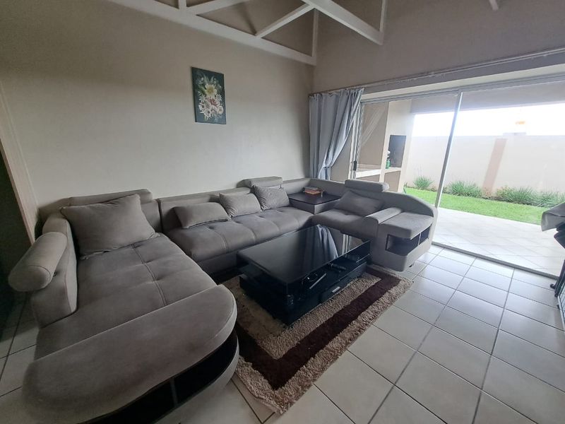 Spacious living room featuring exposed ceiling beams, tiled flooring, and large sliding doors providing seamless access to the outdoor patio and garden area.