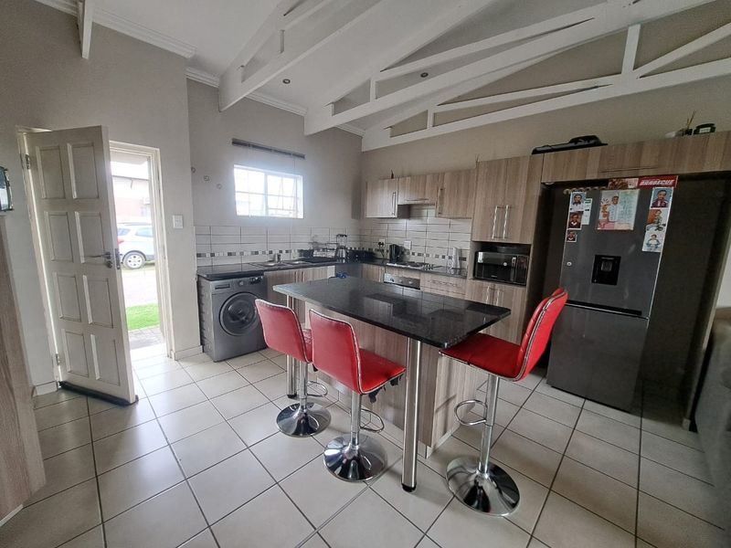 A functional kitchen featuring built-in cabinetry, granite countertops, a central island, tiled flooring, and exposed ceiling beams, with direct access to the exterior.