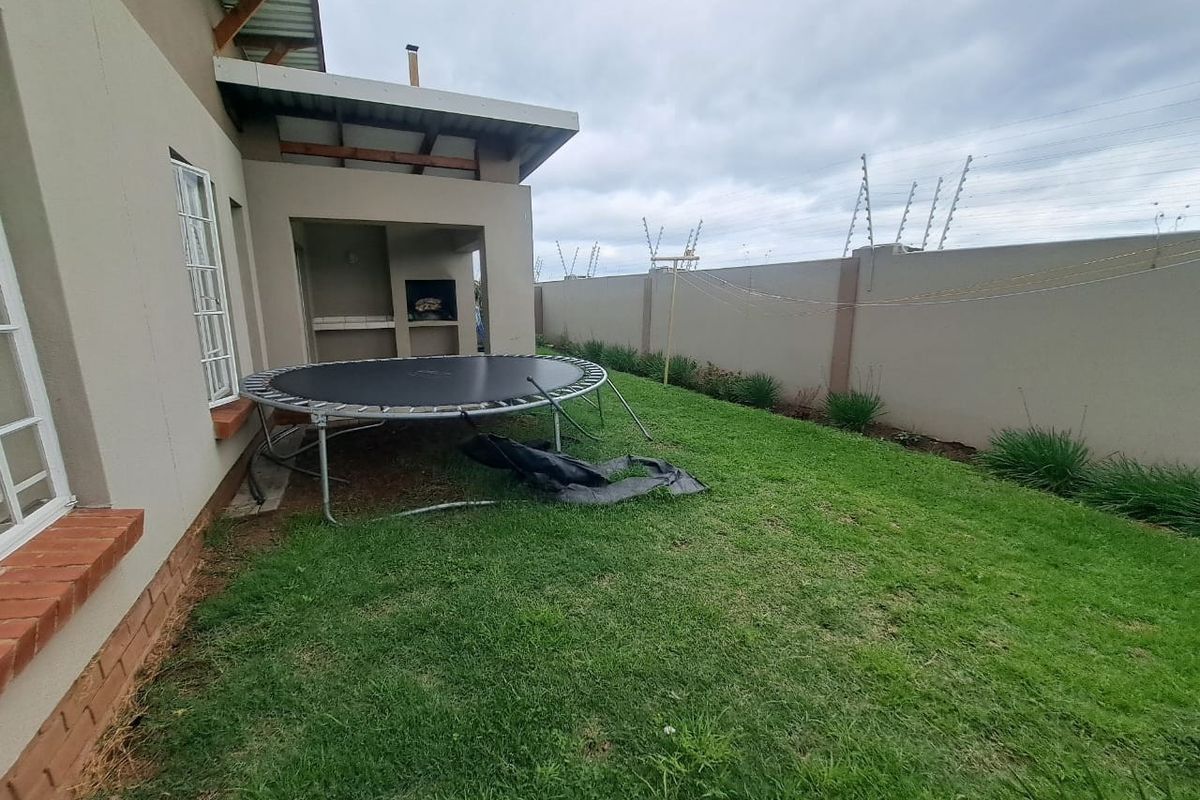 Rear garden area featuring a covered patio with a built-in braai, enclosed by a perimeter wall with electric fencing.