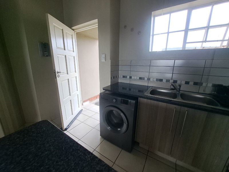 Functional laundry area featuring built-in cabinetry, granite countertops, a double basin sink, and tiled flooring with direct access to the exterior.