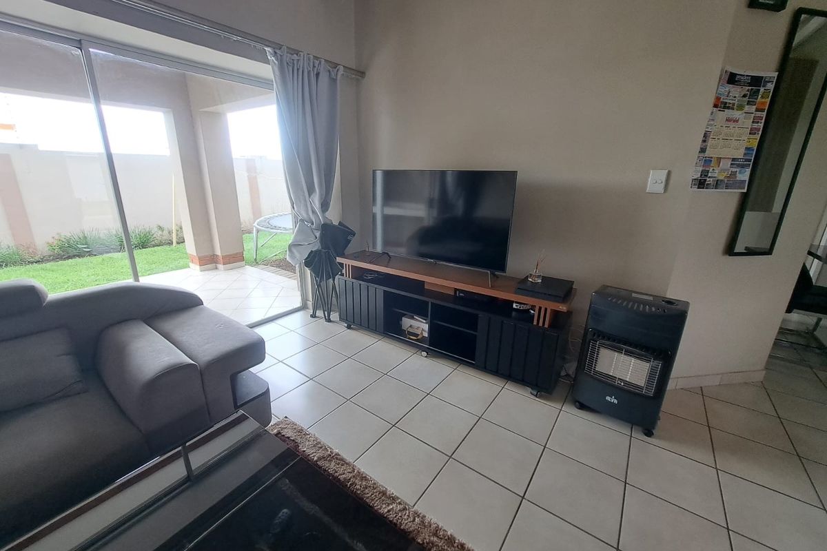 A living room featuring tiled flooring and a large sliding glass door providing direct access to a covered patio and garden area.