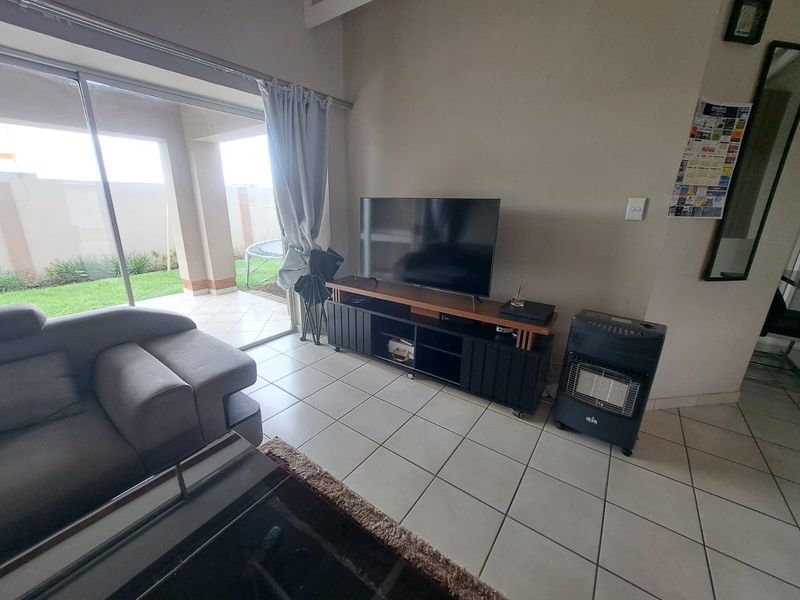A living room featuring tiled flooring and a large sliding glass door providing direct access to a covered patio and garden area.