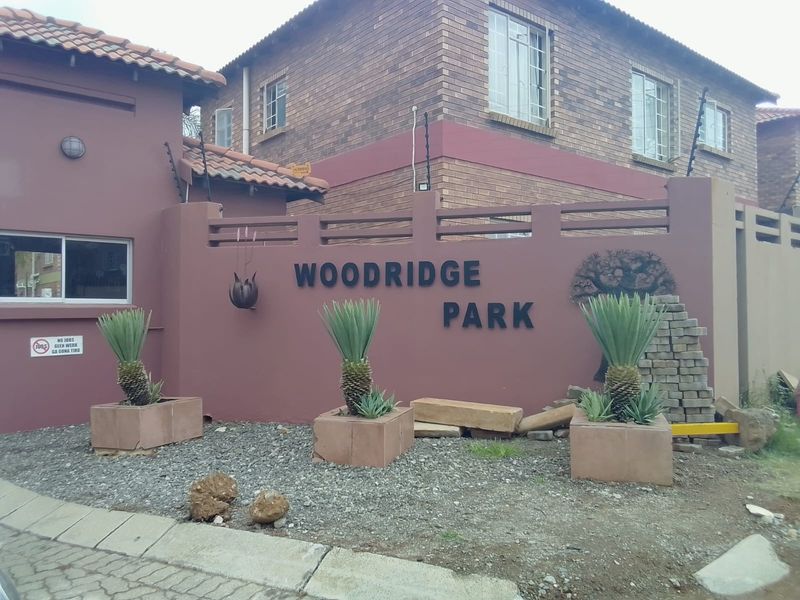 Front entrance view of Woodridge Park apartment complex featuring brick facade, boundary wall with electric fencing, and paved driveway access.