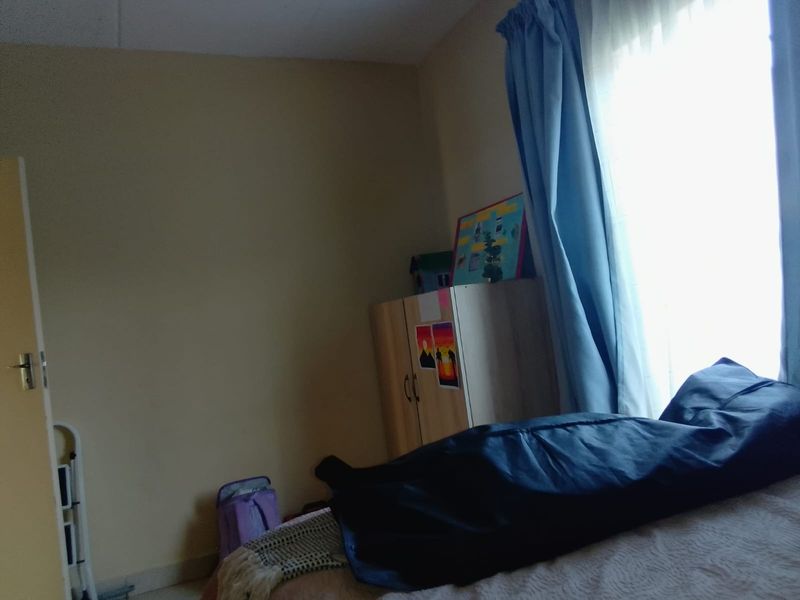 A standard bedroom featuring neutral wall finishes and natural light from a window with curtains.