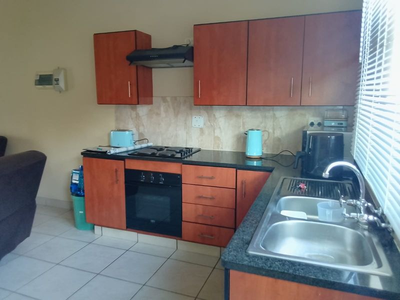 A functional kitchen featuring wooden cabinetry, granite countertops, a built-in oven with hob, and a double bowl sink with tiled splashback.