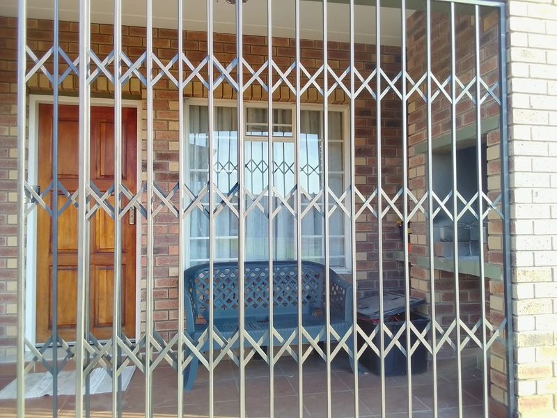 A covered patio area featuring a brick facade, built-in braai, and a secure metal gate entrance.