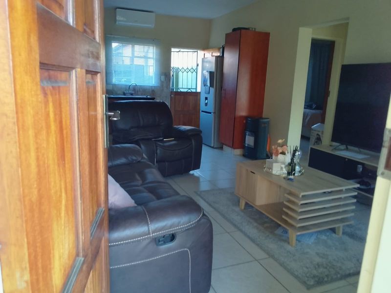 Open-plan living area featuring tiled flooring, a wall-mounted air conditioning unit, and direct access to an exterior security gate.