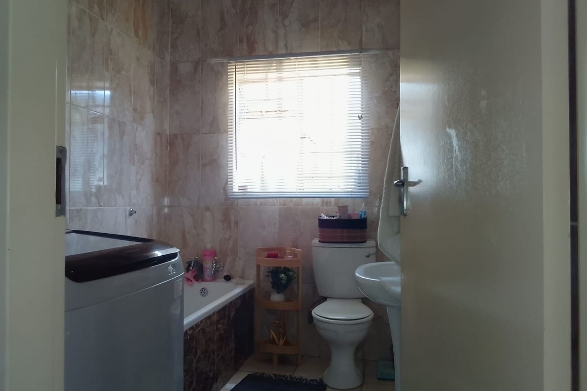 A compact bathroom featuring a bathtub, pedestal basin, and toilet with tiled walls and a window with a venetian blind.