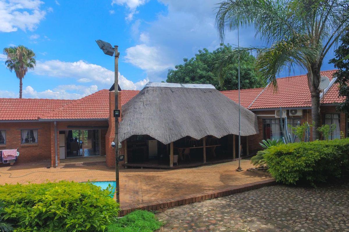 Rear exterior view featuring a brick-paved patio area with a thatched roof lapa, swimming pool, and traditional brick house architecture.