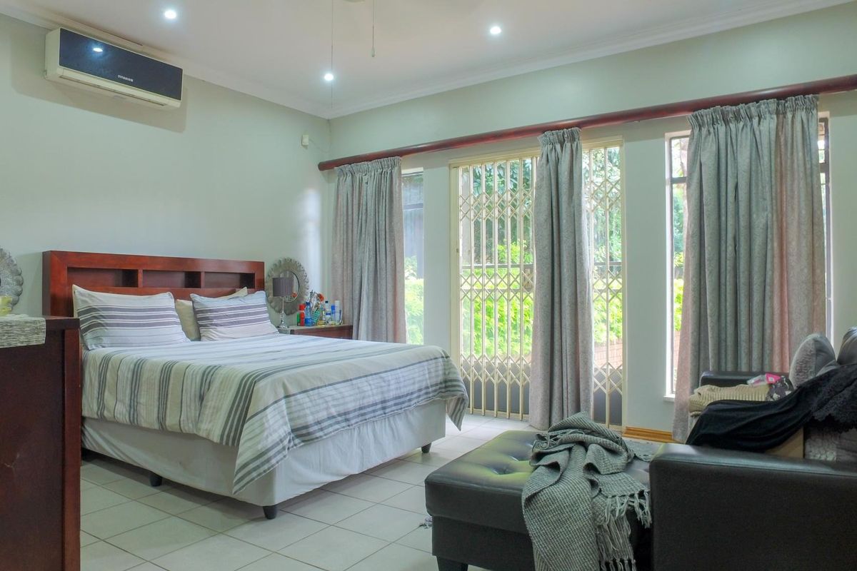Spacious bedroom featuring tiled flooring, recessed downlighting, a wall-mounted air conditioning unit, and direct access to the garden through a secure sliding door.