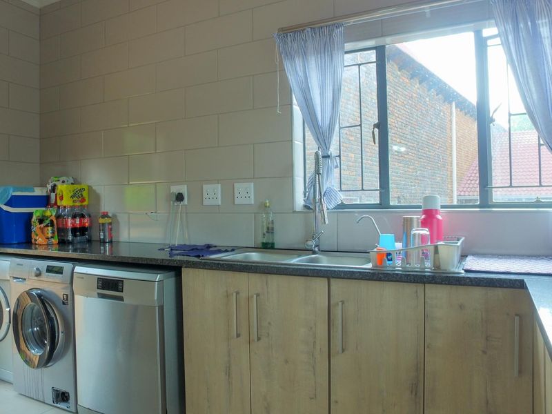 A functional laundry area featuring laminate cabinetry, granite countertops, a double sink, and tiled splashbacks, providing ample space for laundry appliances.