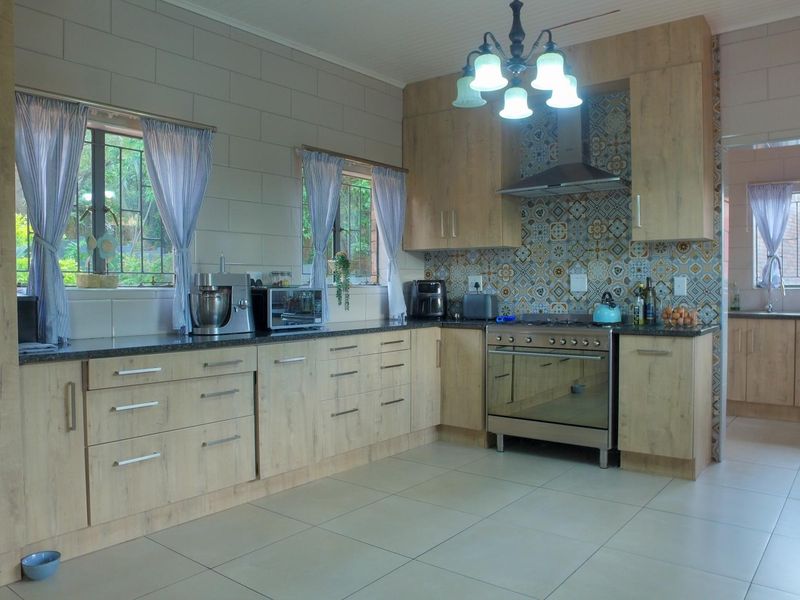 A well-maintained kitchen featuring light wood-finish cabinetry, a decorative tiled splashback, stainless steel oven and extractor fan, and neutral floor tiles.