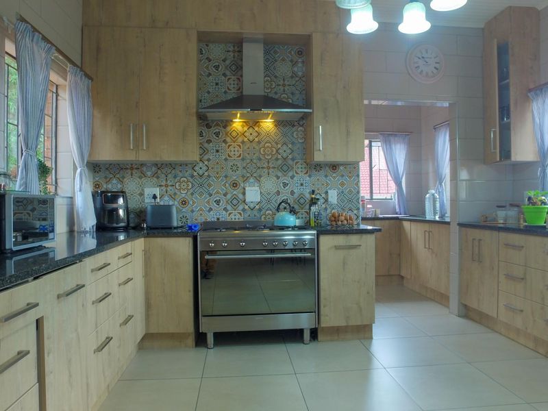 A well-maintained kitchen featuring wood-look cabinetry, granite countertops, a stainless steel gas stove, and decorative patterned tile splashbacks.
