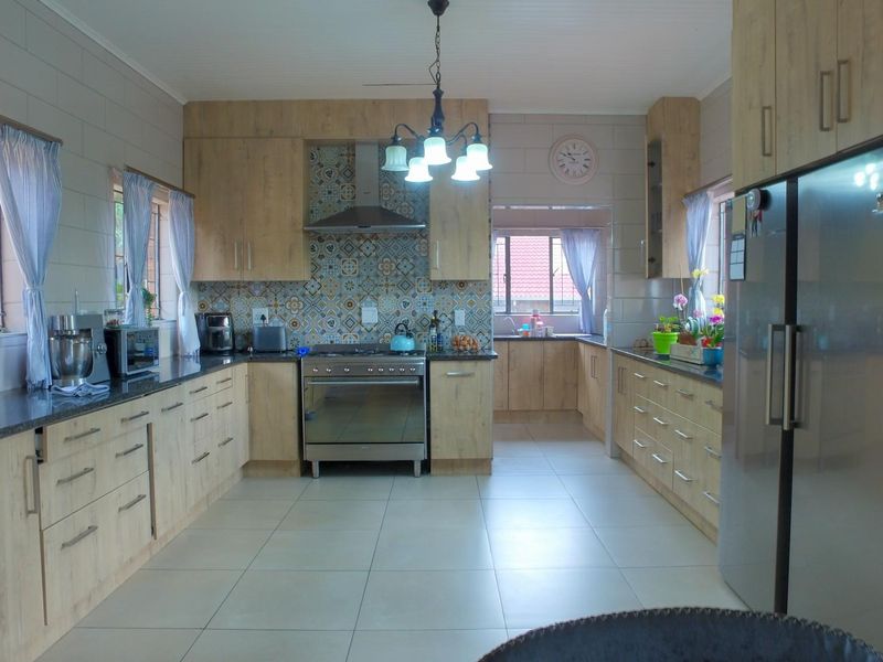 A spacious, well-maintained kitchen featuring light wood-finish cabinetry, stone countertops, a decorative tiled backsplash, and integrated stainless steel appliances.