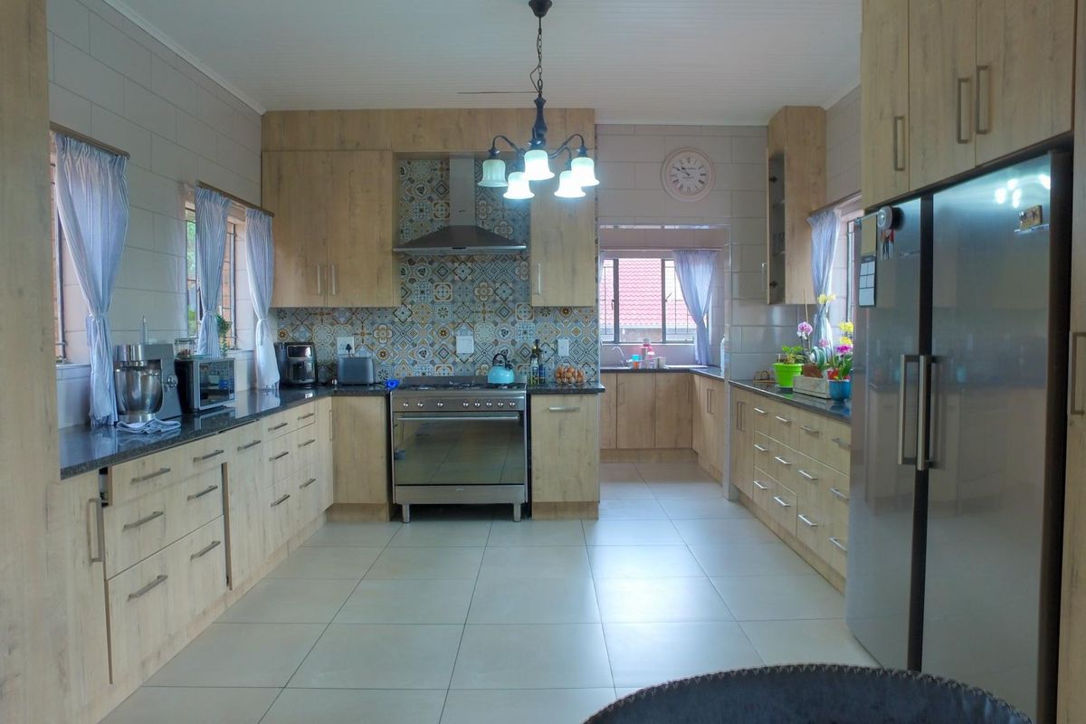 A spacious, well-maintained kitchen featuring light wood-finish cabinetry, stone countertops, a decorative tiled backsplash, and integrated stainless steel appliances.