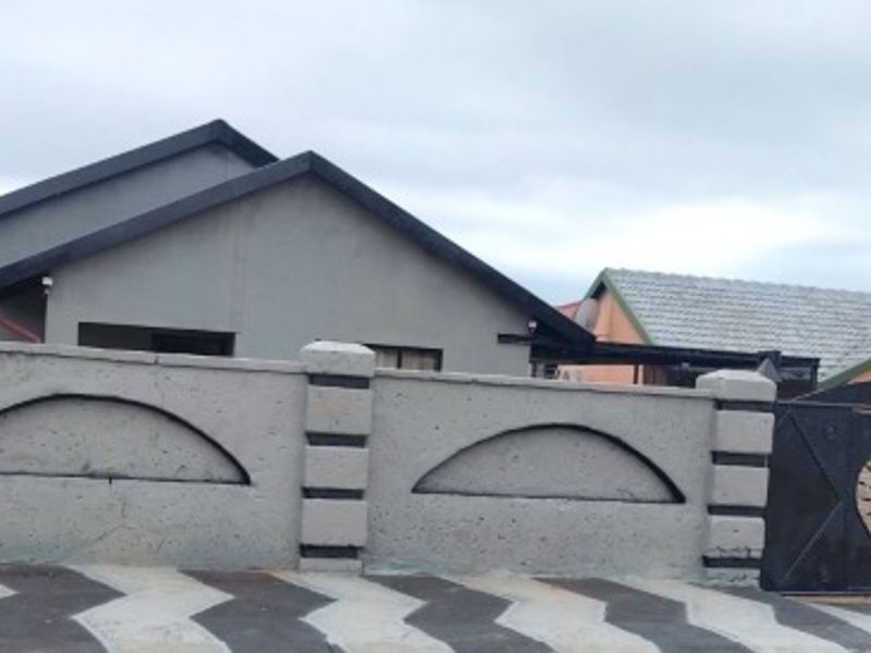 Front view of a residential property featuring a paved driveway, a decorative perimeter wall with a metal gate, and a pitched roof structure.