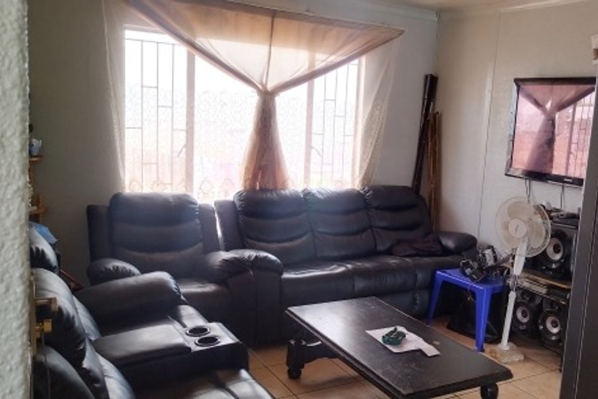A living room area featuring tiled flooring and a large window with security bars, offering a functional space for relaxation.