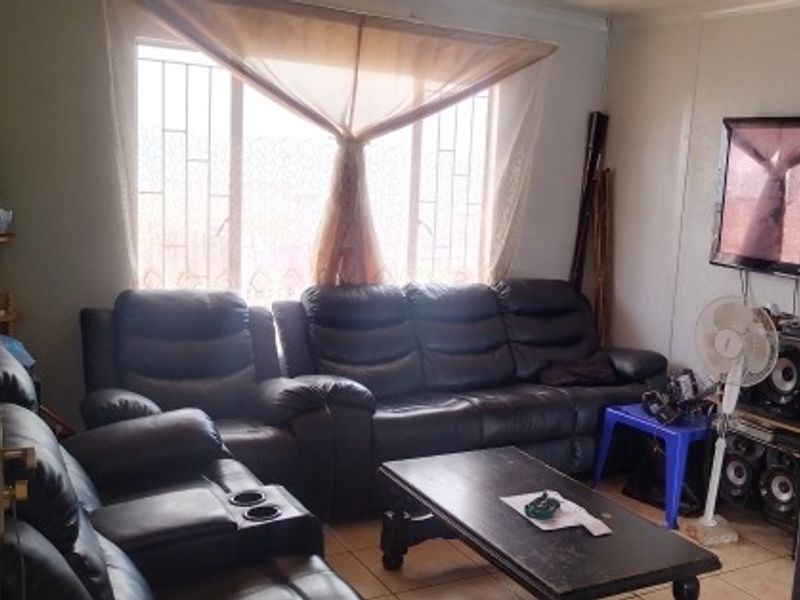 A living room area featuring tiled flooring and a large window with security bars, offering a functional space for relaxation.
