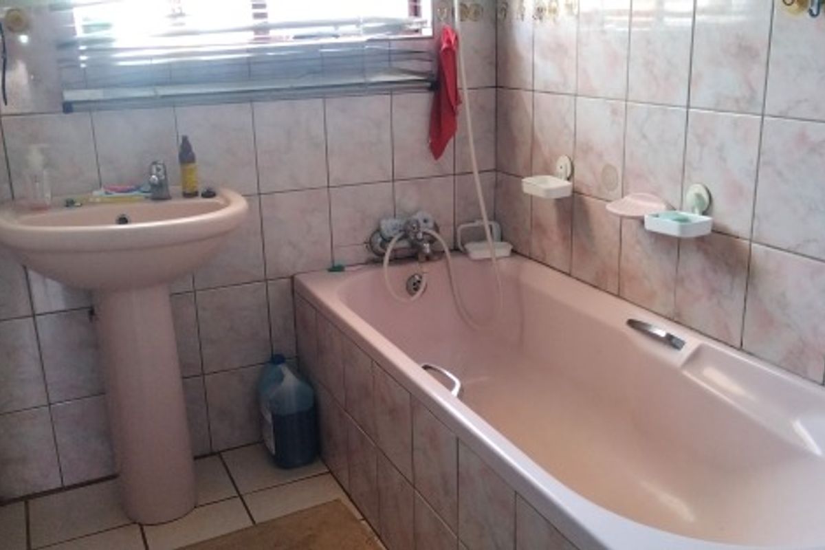 A dated bathroom featuring a pink pedestal basin and matching bathtub with tiled walls and flooring.
