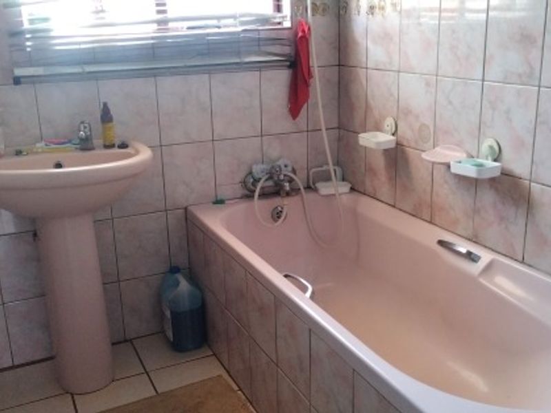 A dated bathroom featuring a pink pedestal basin and matching bathtub with tiled walls and flooring.