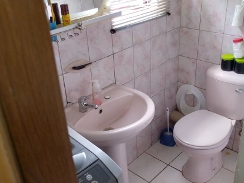 A compact bathroom featuring a pedestal sink, toilet, and fully tiled walls and floors, offering a functional space with potential for modern updates.