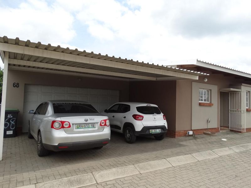 Front exterior view of the townhouse featuring a covered carport, paved driveway, and secure garage access.
