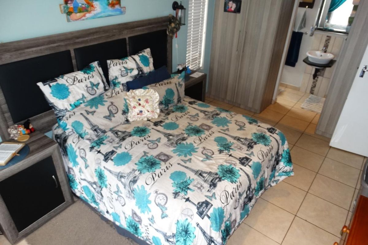 A bedroom featuring built-in cupboards, tiled flooring, and an en-suite bathroom, offering a functional layout with neutral finishes.
