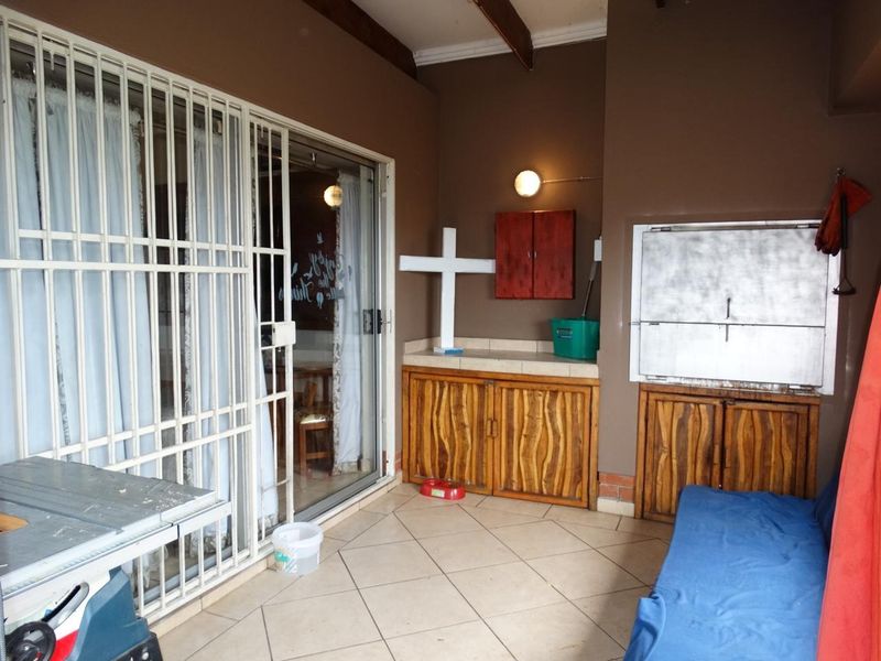 Covered patio area featuring a built-in braai, tiled flooring, and direct access to the interior through sliding glass doors with security gates.
