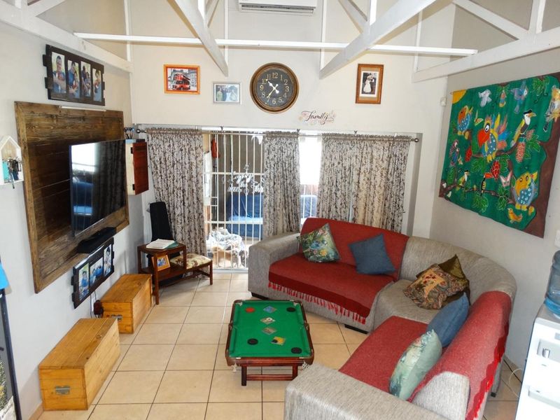 A living room featuring exposed white roof trusses, ceramic floor tiling, and a security gate leading to an outdoor area.