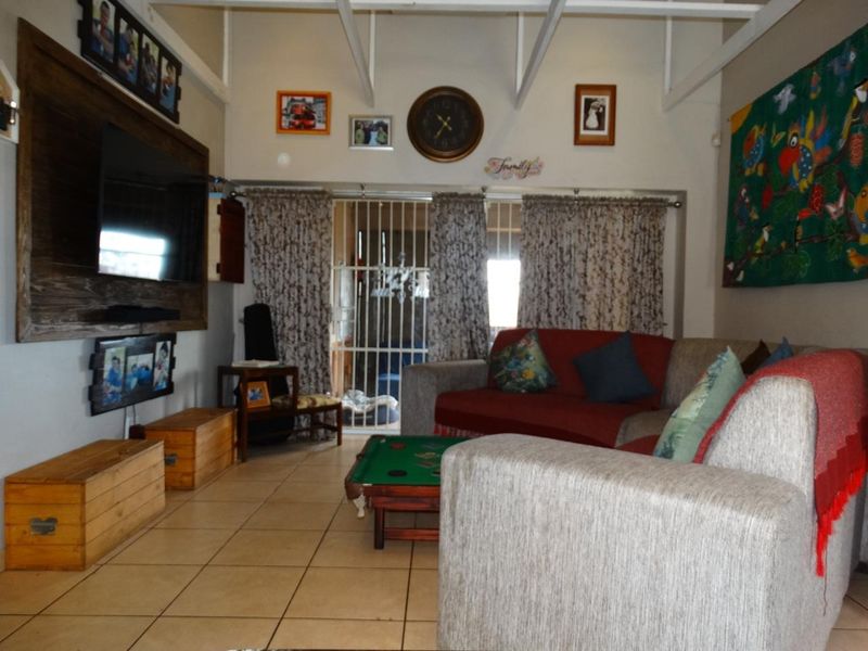 A living room featuring exposed ceiling beams, tiled flooring, and a security gate leading to an outdoor area.