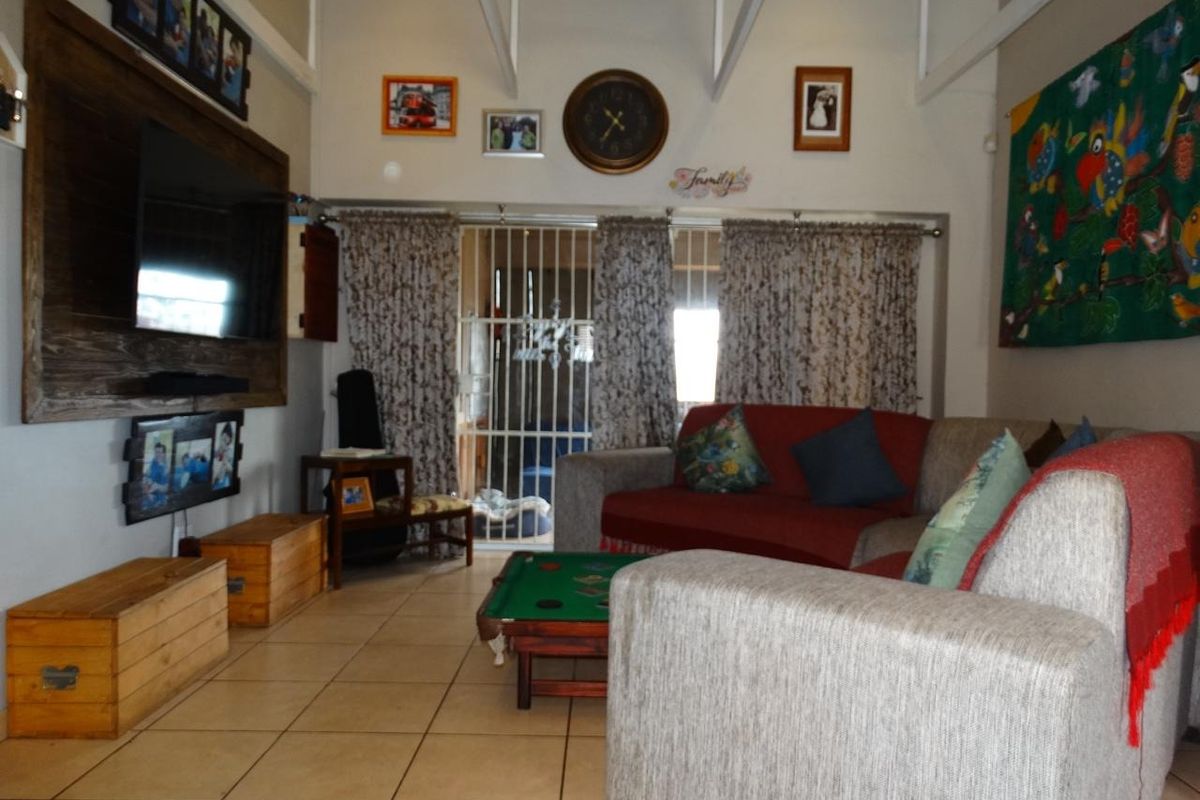 A living room featuring exposed ceiling beams, tiled flooring, and a security gate leading to an outdoor area.