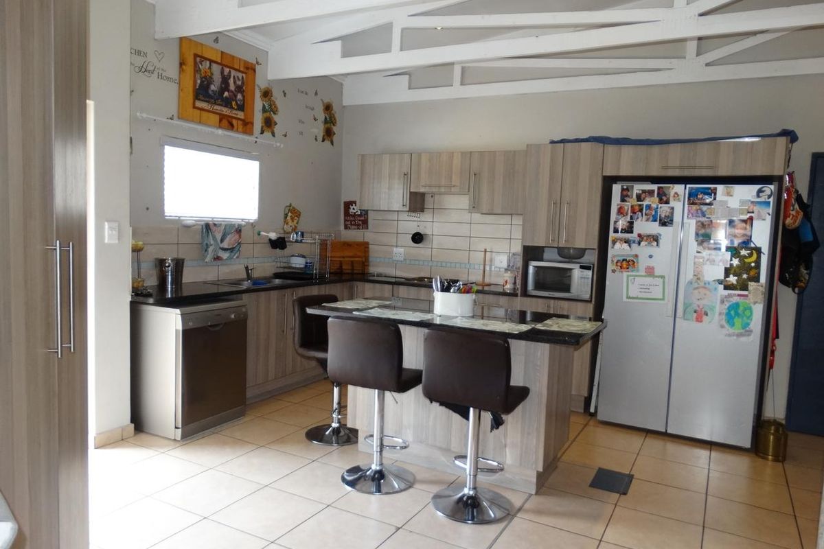 A functional kitchen featuring light wood-finish cabinetry, granite countertops, a central island, and exposed white roof trusses, providing a bright and open workspace.