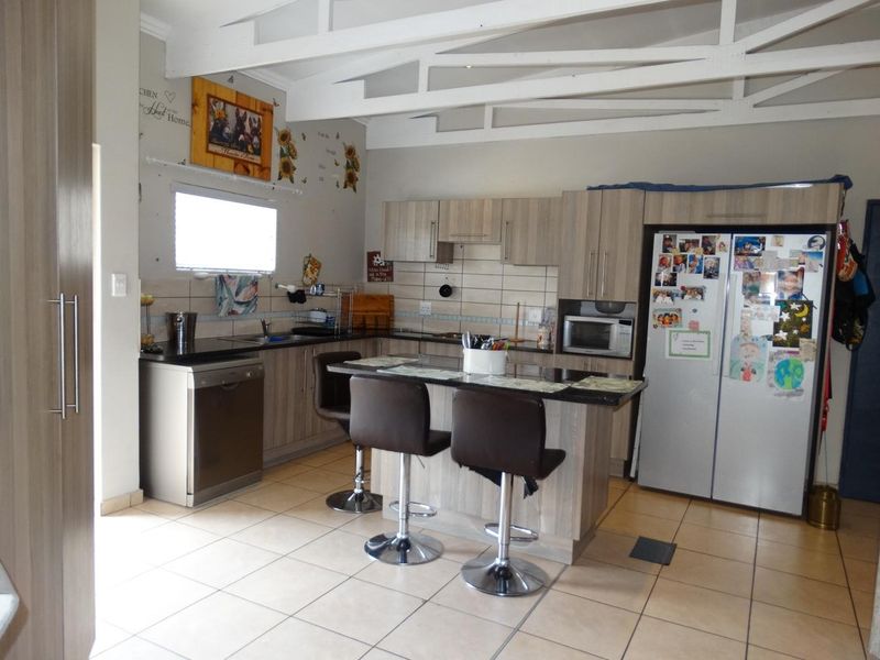 A functional kitchen featuring light wood-finish cabinetry, granite countertops, a central island, and exposed white roof trusses, providing a bright and open workspace.