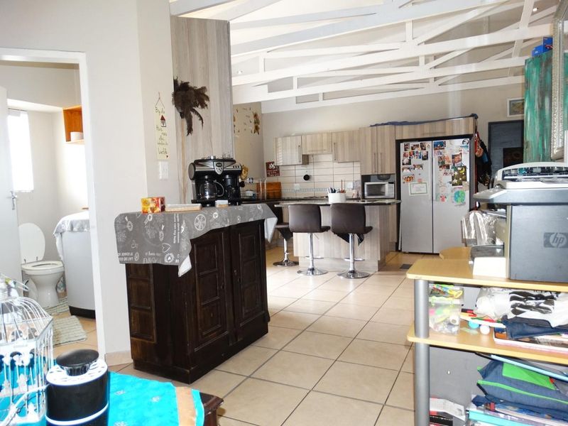Open-plan kitchen and living area featuring tiled flooring, exposed ceiling beams, and a central kitchen island with breakfast bar seating.
