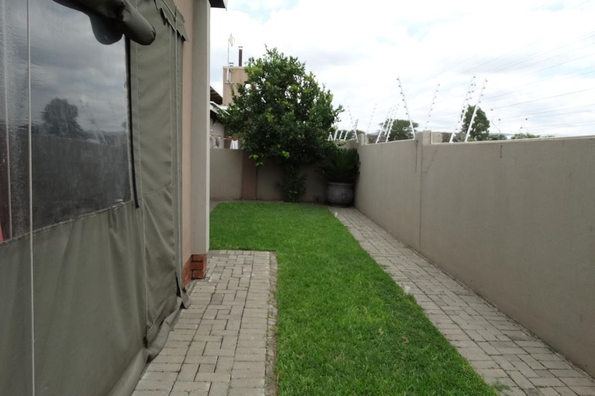 A private rear garden featuring a paved walkway, a small lawn area, and a boundary wall secured with electric fencing.