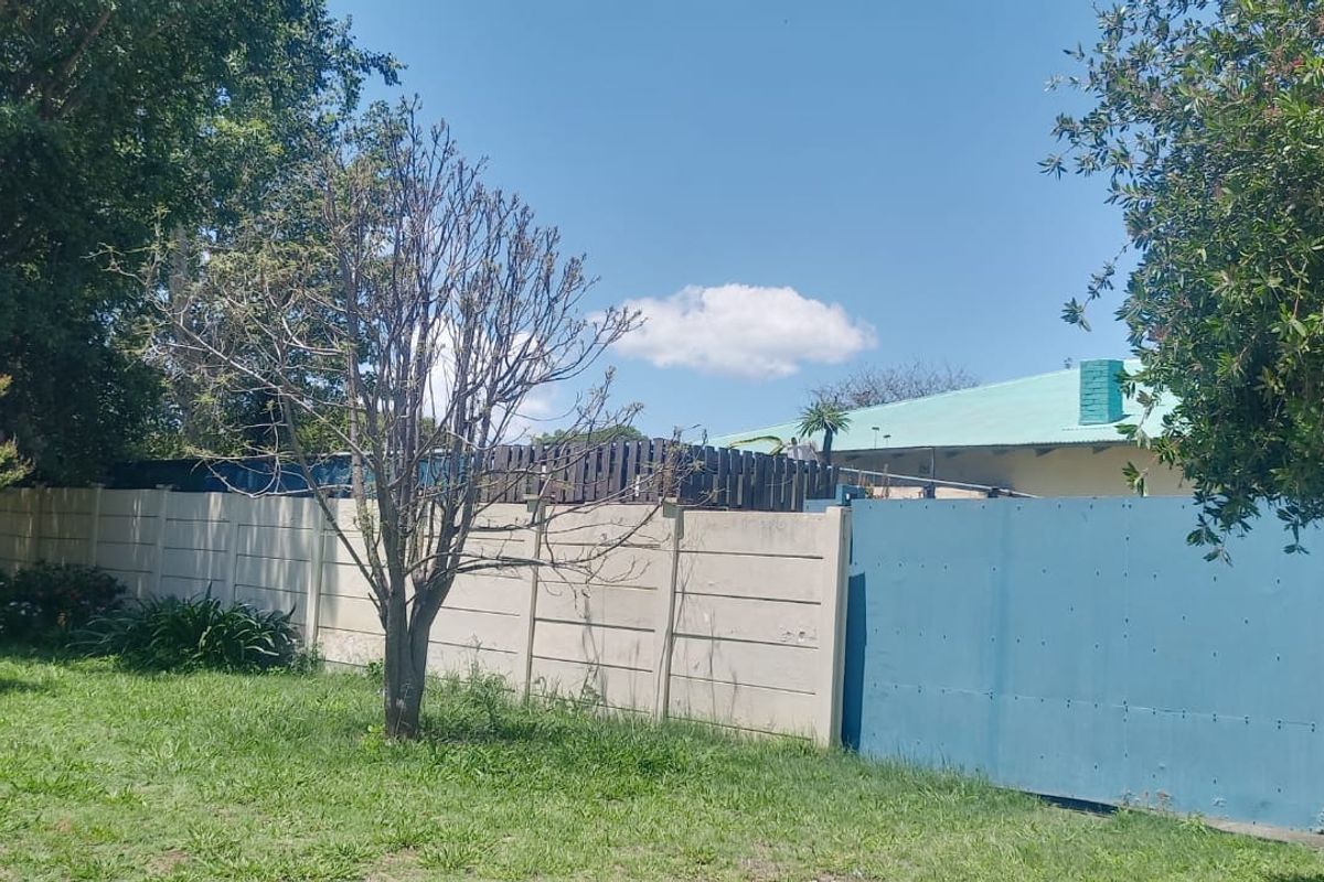 Front exterior view showing a precast concrete boundary wall and a blue metal driveway gate with a pedestrian entrance.