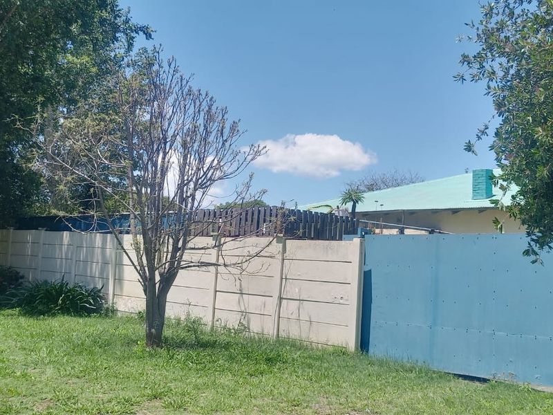 Front exterior view showing a precast concrete boundary wall and a blue metal driveway gate with a pedestrian entrance.