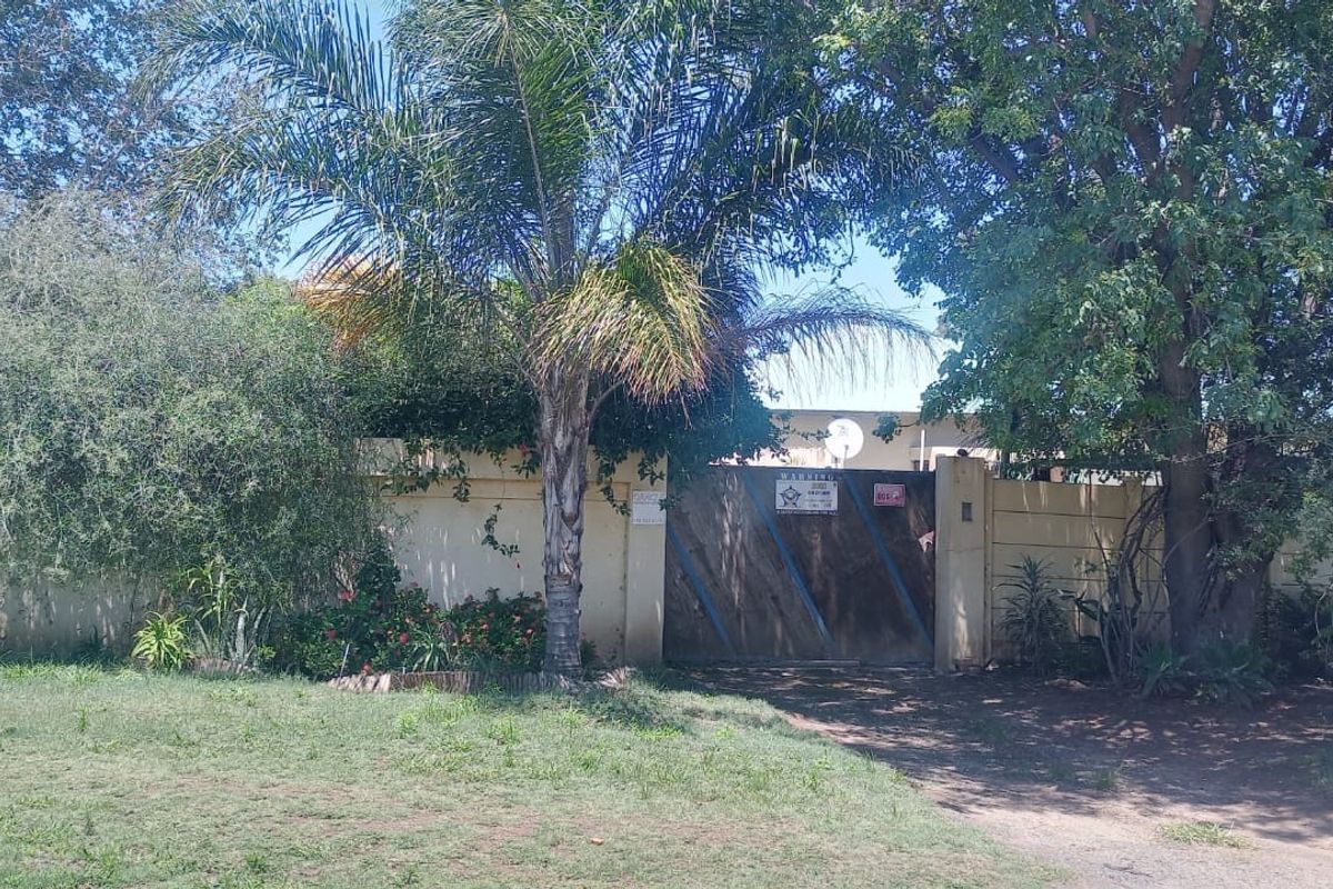 Front view of the property featuring a secure entrance gate, boundary wall, and established garden area.