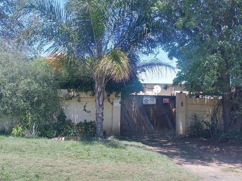 Front view of the property featuring a secure entrance gate, boundary wall, and established garden area.