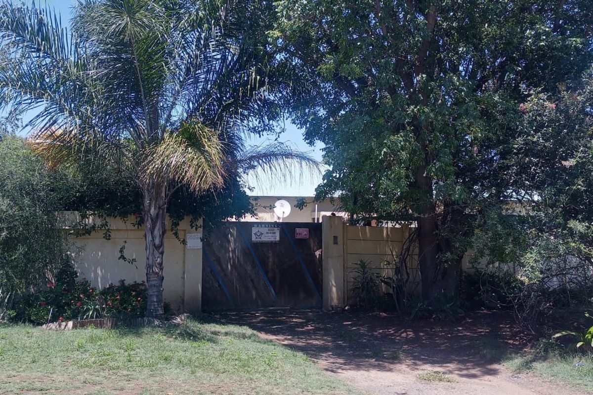 Front view of the property featuring a solid timber gate, boundary wall, and mature garden landscaping.