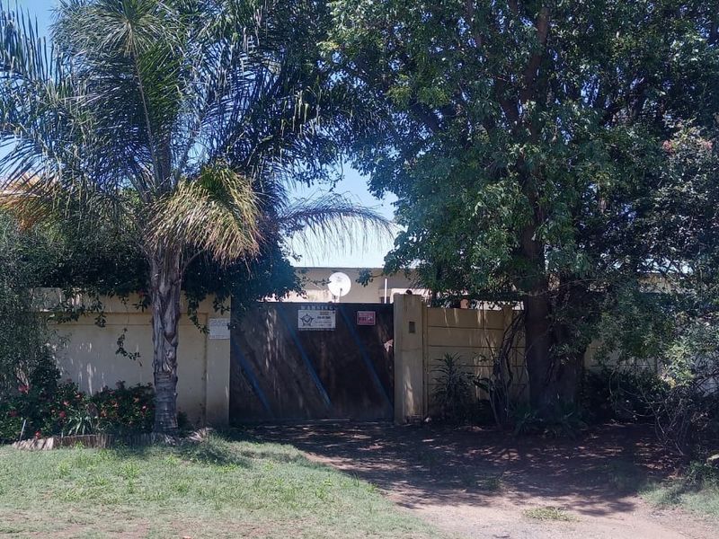 Front view of the property featuring a solid timber gate, boundary wall, and mature garden landscaping.