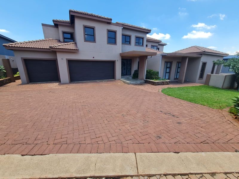 A well-maintained double-story residential property featuring a spacious paved driveway, double garage, and a covered entrance with a neat front garden.