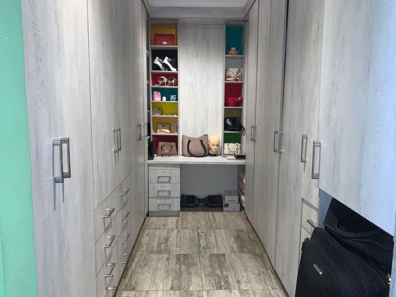 A walk-in closet featuring extensive built-in cabinetry with light wood-grain finish, integrated vanity area, and tiled flooring.