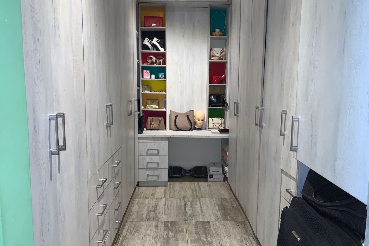 A walk-in closet featuring extensive built-in cabinetry with light wood-grain finish, integrated vanity area, and tiled flooring.