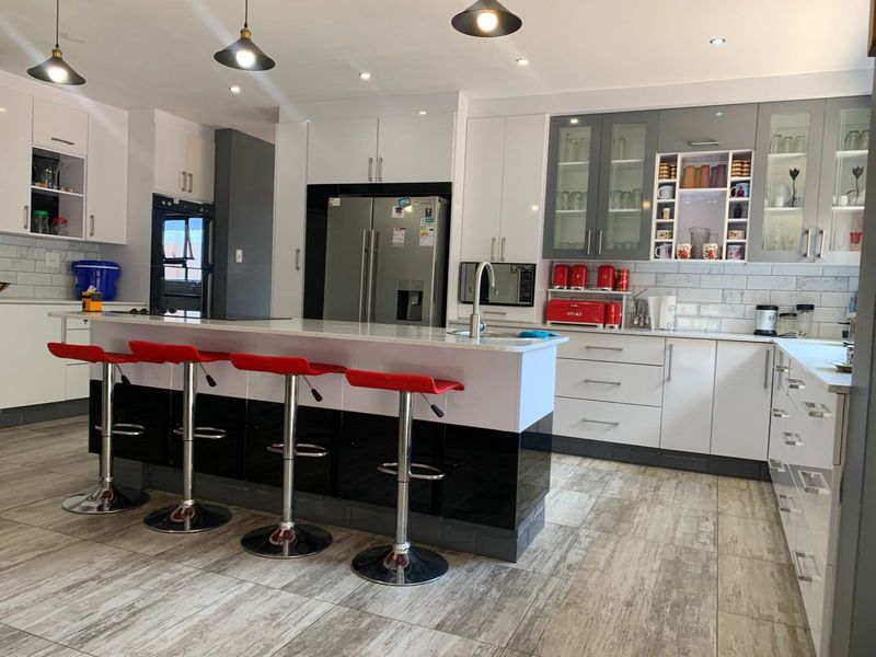 Modern kitchen featuring a central island, high-gloss cabinetry, stone countertops, integrated appliances, and stylish pendant lighting with a neutral tiled floor.