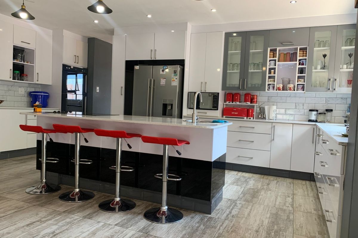 Modern kitchen featuring a central island, high-gloss cabinetry, stone countertops, integrated appliances, and stylish pendant lighting with a neutral tiled floor.