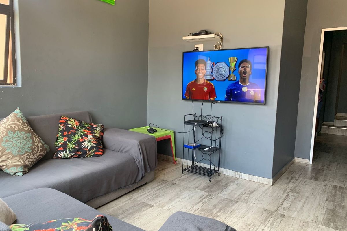 A living room featuring grey painted walls and light-toned tiled flooring, equipped with a wall-mounted television.