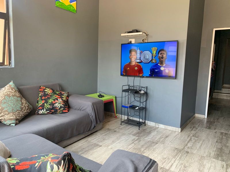 A living room featuring grey painted walls and light-toned tiled flooring, equipped with a wall-mounted television.